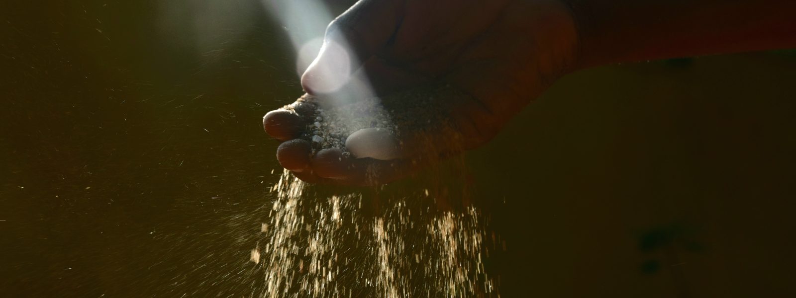 sand trickling out of a hand against a dark brown backdrop