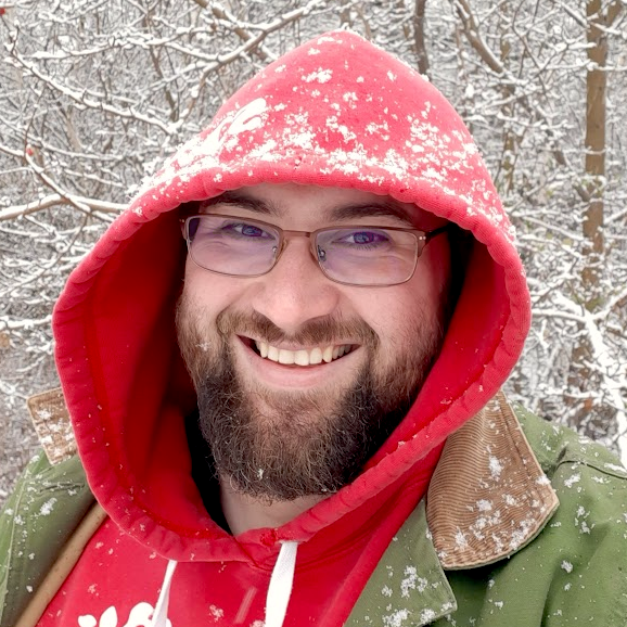 Jonathan Olfert is smiling, has a beard, and is wearing glasses a red hoodie