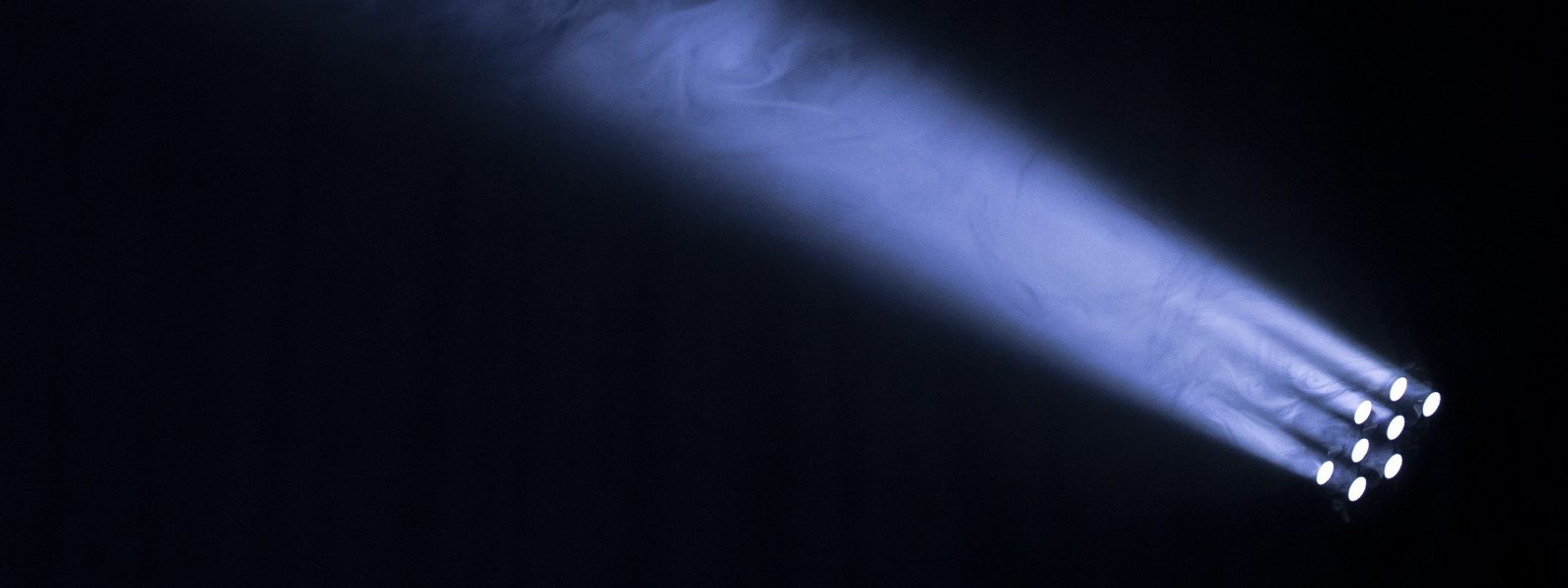 spotlights and fog, lit up blue, forming a ray of illumination from bottom right to top left against a dark background