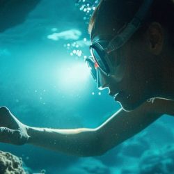 a girl diving underwater, reaching out for an object